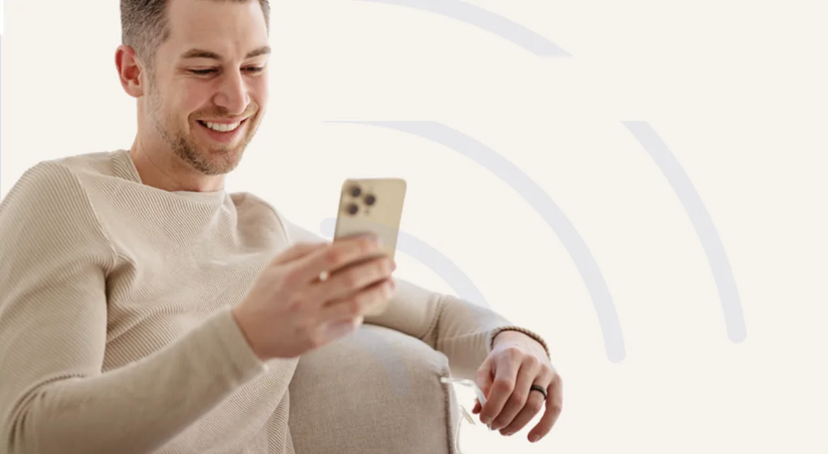 Homem sorrindo enquanto usa o celular no sofá